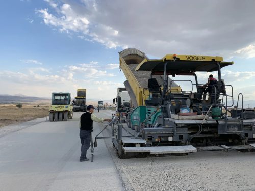 Frig Vadisi Emre Gölü turizm yolu çalışmasında, finişere malzeme boşaltan damperli kamyonumuz, yol silindirleri ve serim ekibinin görünümü.