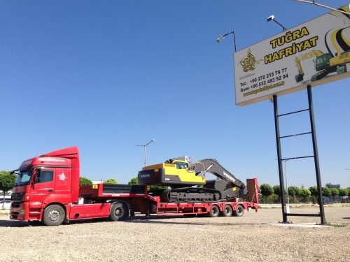 Tuğra Hafriyat garajında kırmızı Mercedes çekicimize bağlı lowbed dorsesinde yüklü Volvo ekskavatörümüz ve sağ üstte firmamızın tabelası.