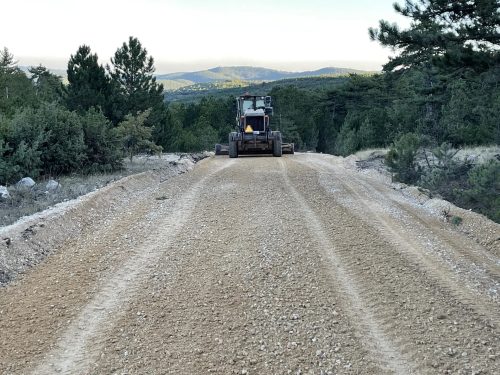 Eskişehir Kırka yakınındaki mermer ocağı yolunda, çam ağaçları arasında 0–38 agrega serilmiş yol yüzeyini tesviye eden greyderimizin görünümü.